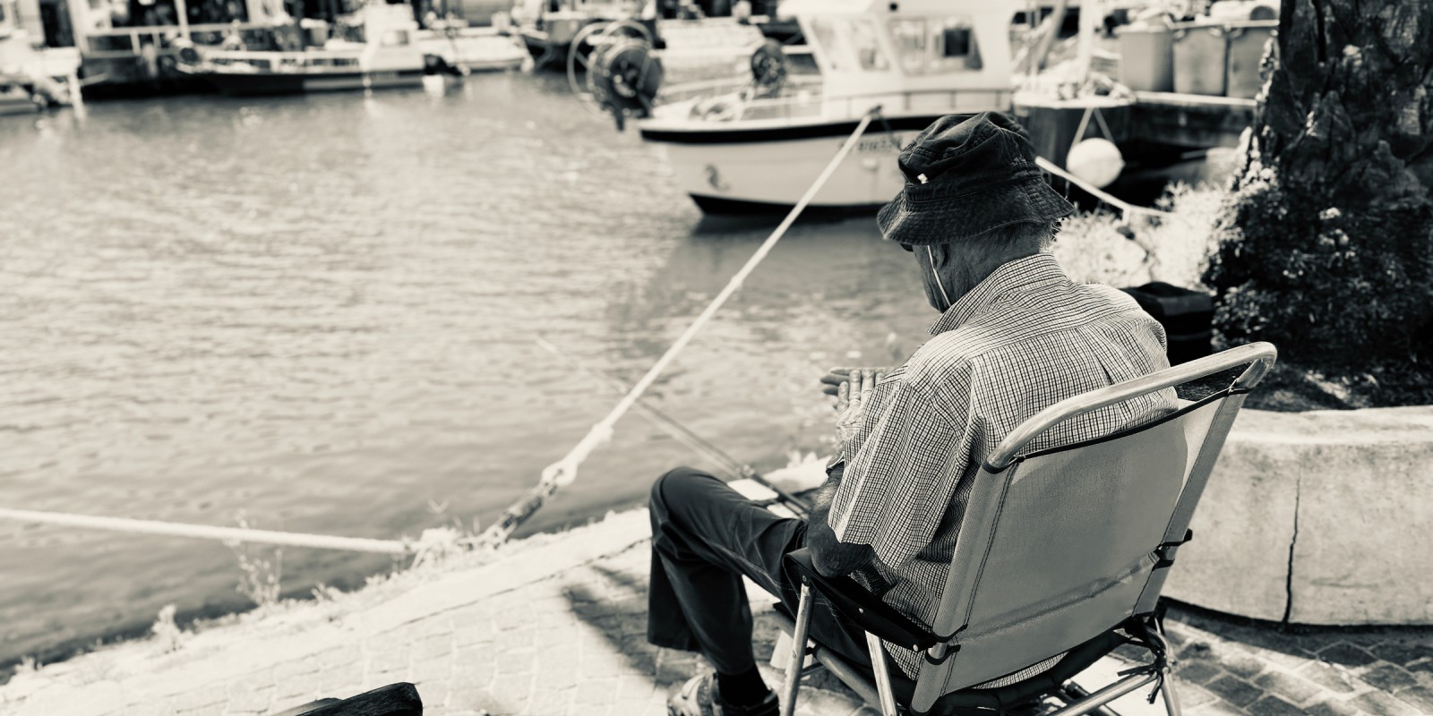 Traces de l'ancien temps : Un peu d'ombre, une chaise pliante, une canne à pêche, bien sûr un bob, le vieil homme profite d'une matinée paisible
