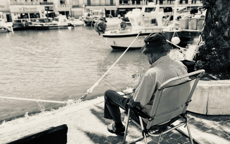 Traces de l'ancien temps : Un peu d'ombre, une chaise pliante, une canne à pêche, bien sûr un bob, le vieil homme profite d'une matinée paisible